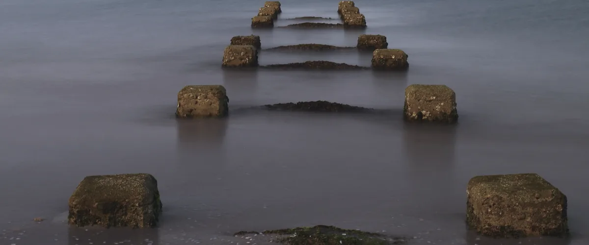 Weathered stone foundations of an old jetty standing in calm, misty water